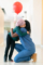 A beautiful African American girl with cancer is wearing a headscarf. She is in wearing the hospital corridor. Her kind female doctor is kneeling down and holding a red ballon to cheer her up. The girl is thanking the doctor for the gift with a big hug.